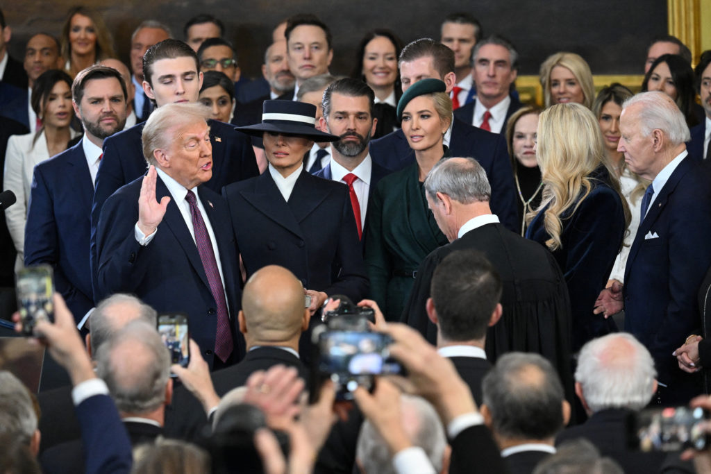 Donald Trump takes the oath of office, administered by Chief Justice John Roberts. Watching on are his family, Vice President JD Vance, other Trump allies, former President Joe Biden, and many other politicians.